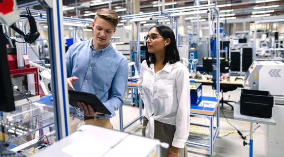 Zwei Azubis mit digitalem Endgerät bei Prüfarbeiten in der Werkhalle.