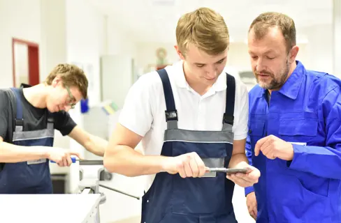 Zwei Praktikanten mit ihrem Ausbilder in einem Metallbetrieb